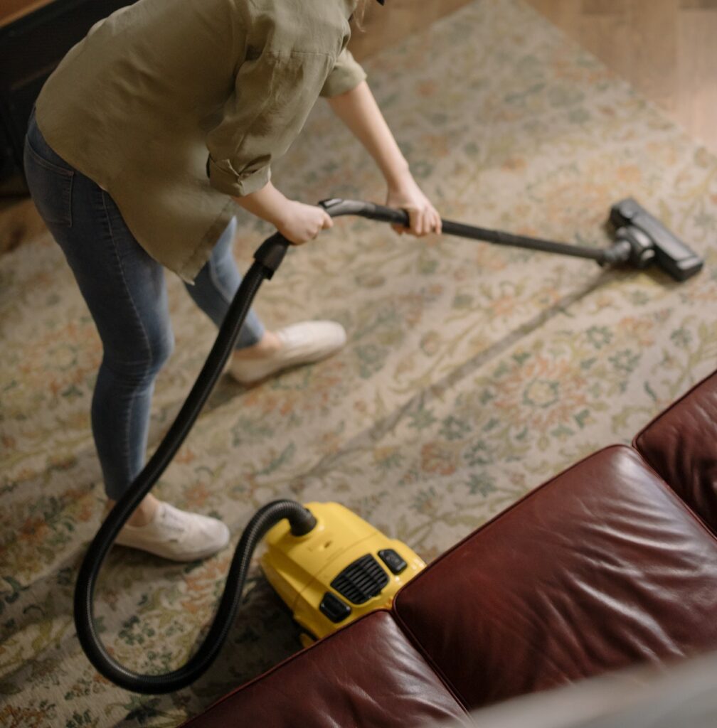 A person vacuuming on the couch with a vacuum.